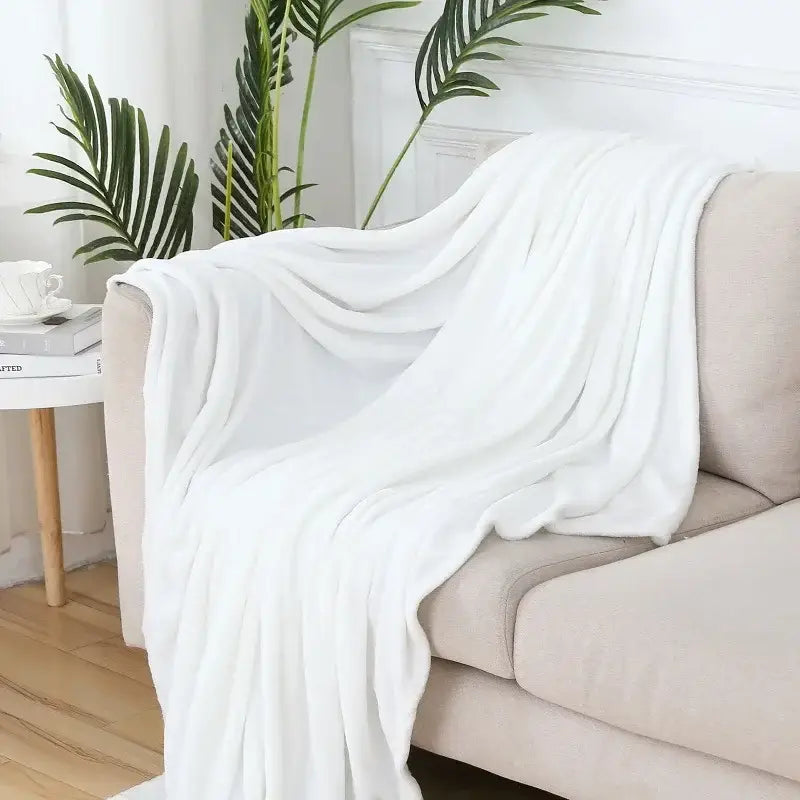 A soft white plush throw blanket draped over a beige sofa arm featuring decorbites cozy flannel warm texture