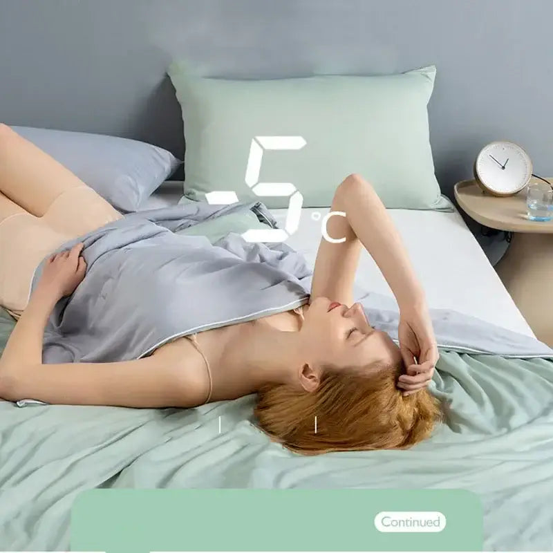 A woman lies on a bed with light gray silk pajamas under a soft mint green decorbites cooling quilt comforter