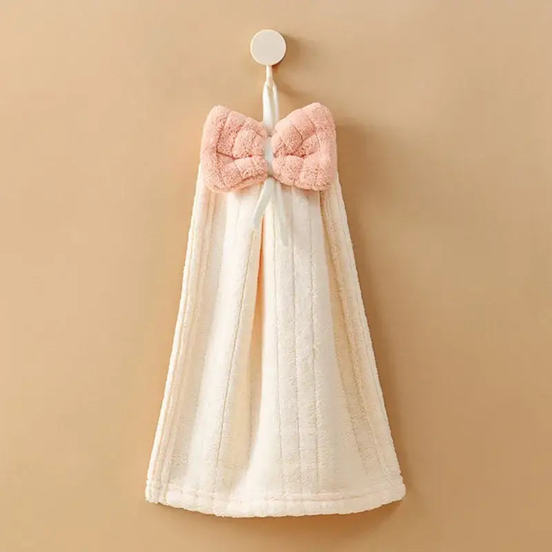 A soft off-white decorbites bowknot microfiber hand towel with a plush pink bow hangs from a hook for kitchen and bathroom