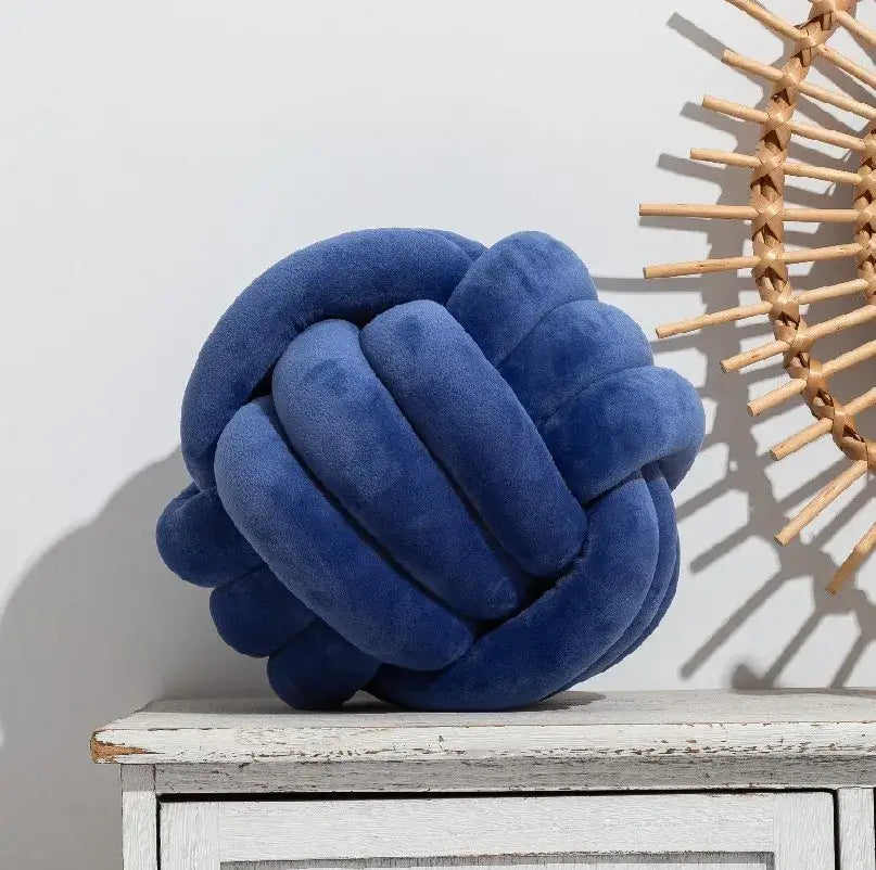 A plush deep blue velour knotted ball round cushion shaped like a knot for bedroom decor