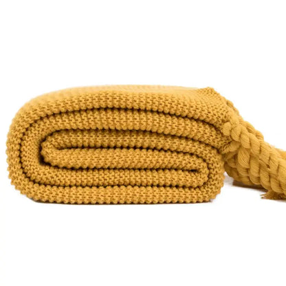 A neatly rolled mustard-yellow decorbites knit throw blanket with a ribbed pattern and braided rope handle