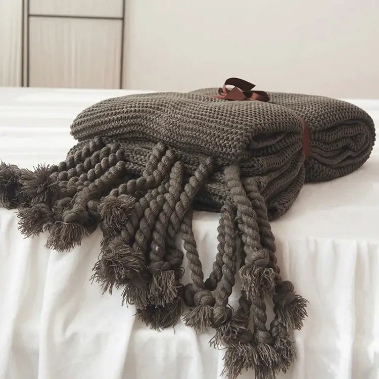 A cozy dark gray decorbites knit throw blanket with thick braided tassels and a brown ribbon tie for living room decor