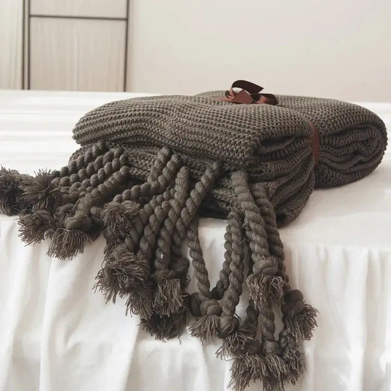 A cozy dark gray decorbites knit throw blanket with thick braided tassels and a brown leather tie for bedroom decor