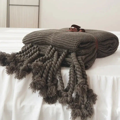 A cozy dark gray decorbites knit throw blanket with thick braided tassels and a brown leather tie for bedroom decor