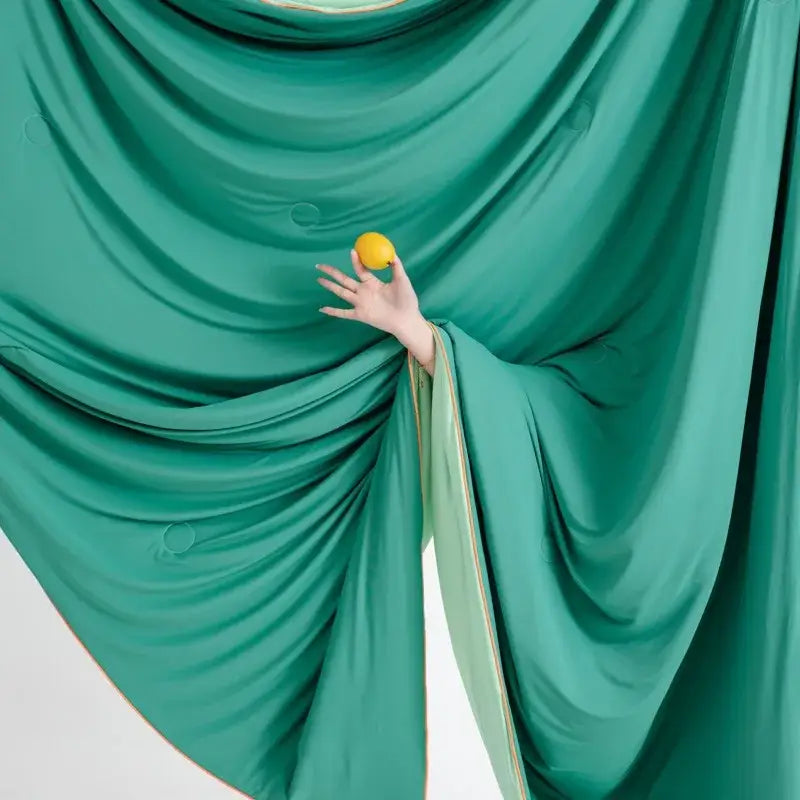 A hand holds a bright yellow lemon against emerald-green satin beside a soft teal and gold decorbites cool fibre summer quilt