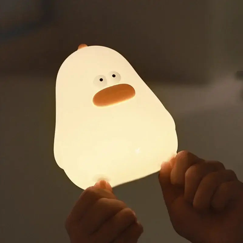 A soft yellow silicone fat chicken night light shaped like a glowing white duck with an orange beak and eyes
