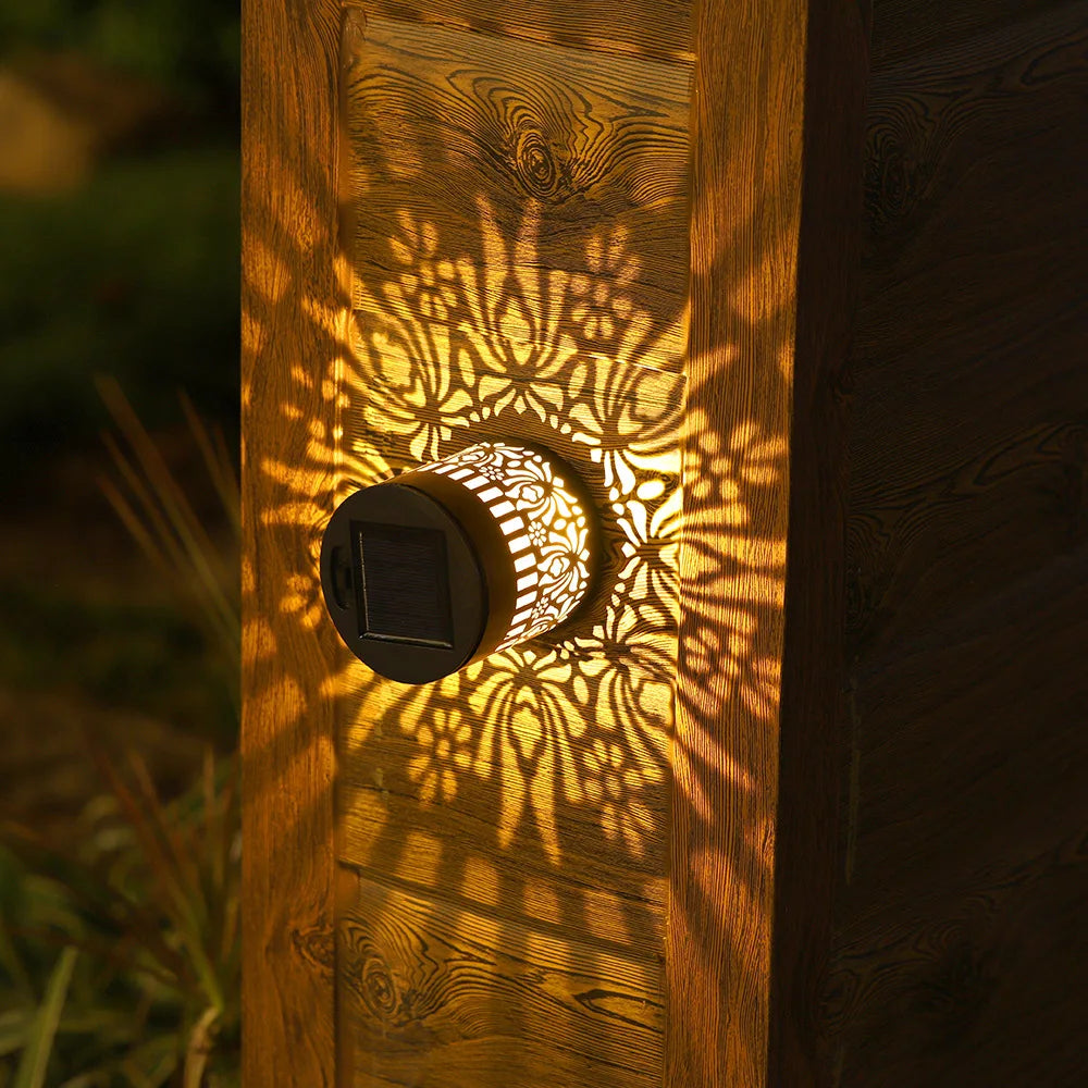 A warm glowing solar-powered datura lantern with intricate cut-out patterns casting shadows on wooden siding