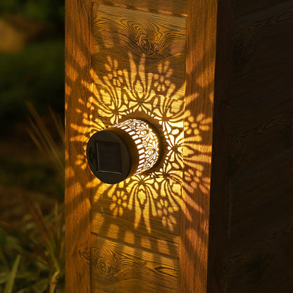A warm glowing solar-powered datura lantern with intricate cut-out patterns casting shadows on wooden siding