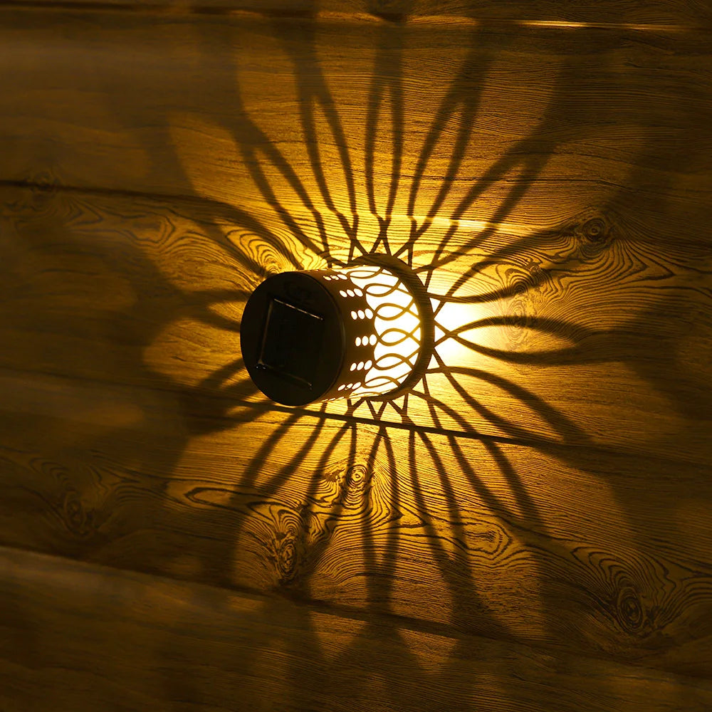 Black solar-powered datura lantern with intricate cut-out patterns casting sunburst shadows on wooden surface for outdoor garden decor
