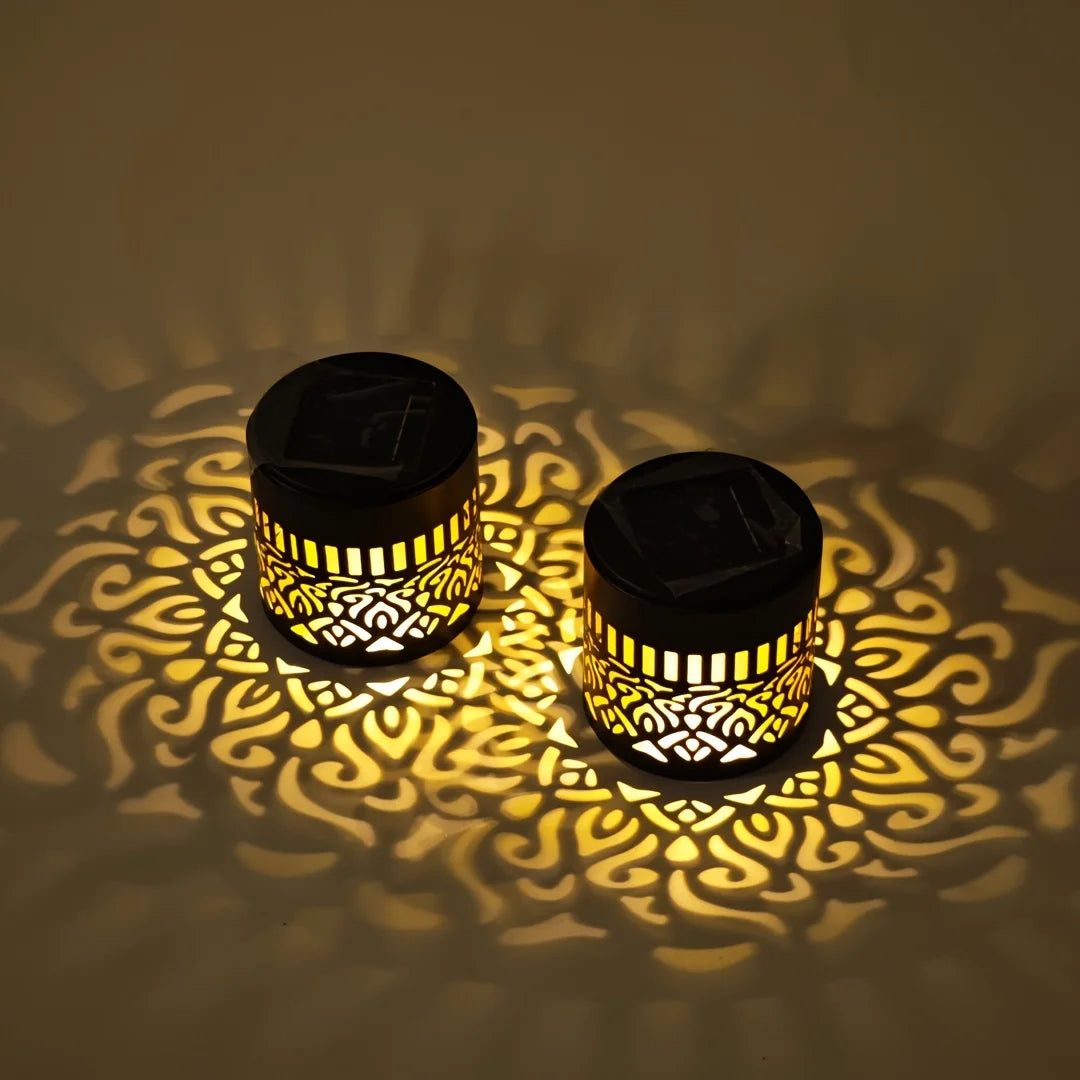 Two black solar-powered datura lanterns with intricate golden cut-out patterns casting warm shadows for garden decor