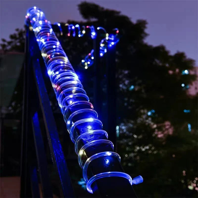 A glowing blue solar led rope light with clear spiral bulbs wrapped around a dark outdoor railing for garden use