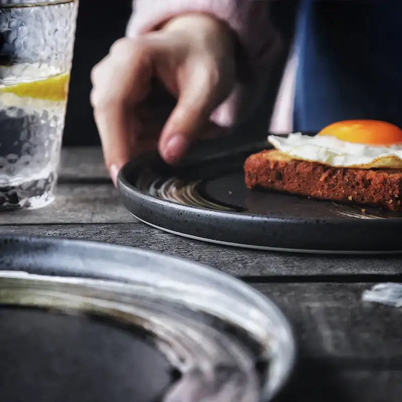 Dark gray decorbites ceramic round dinner plate with subtle rings holding toasted bread topped with sunny-side-up egg