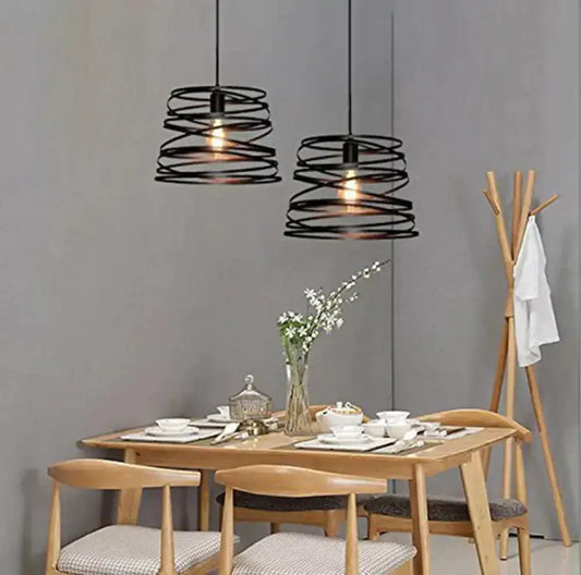 Two black wrought iron spiral spring suspension pendant lights hang above a wooden dining table in a dining room