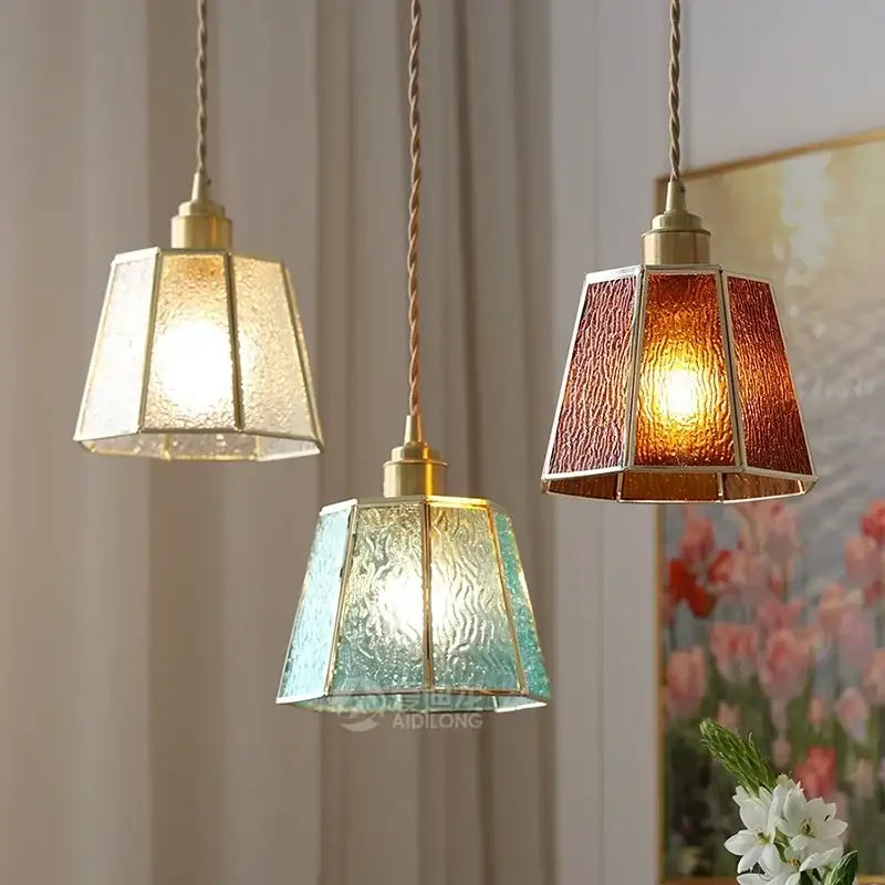 Three hanging pendant lights with colorful glass shades in amber teal and clear framed by brass accents in copper finish