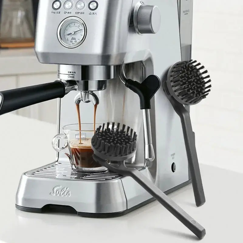 Silver stainless steel solis espresso machine brewing dark coffee with black handle alongside stainless steel coffee maker brush