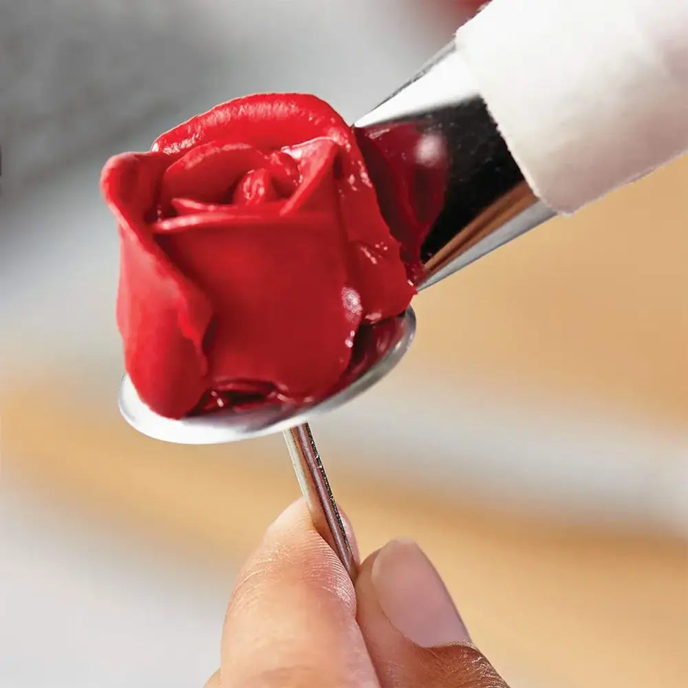 A vibrant red icing rose being piped from a stainless steel cake piping nail set for pastry decorating