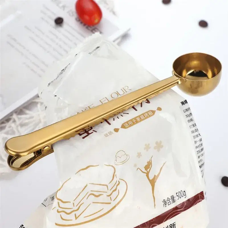 Gold-colored stainless steel coffee spoon with sealing clip designed for precise portioning of dry ingredients