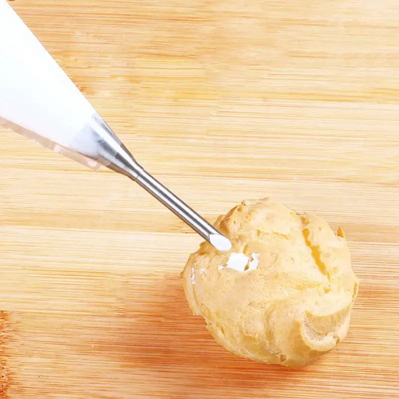 A white stainless steel puff cream nozzle from the dessert puff cream nozzle set applying frosting on choux pastry