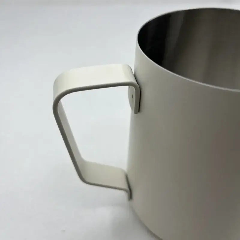 Cream-colored stainless steel milk frothing jug with measurements and minimalist modern design for milk frothing use