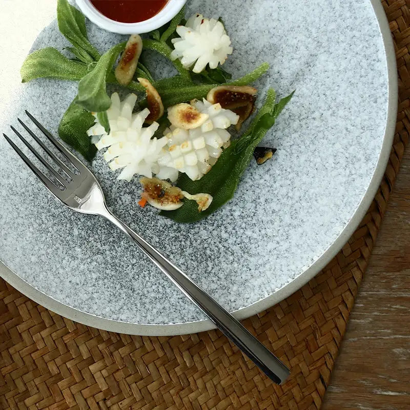 A sleek silver stainless steel fork rests on a stone inspired speckled ceramic dinner plate from decorbites dinner plate set