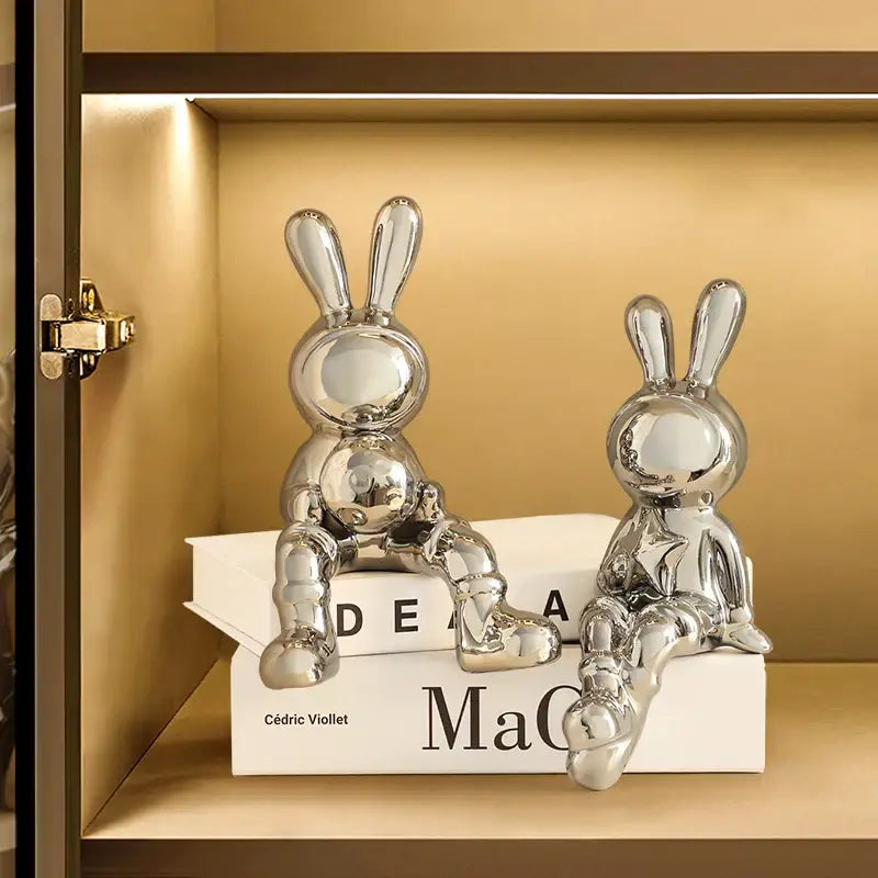 Two sleek chrome ceramic rabbit sculpture set with glossy surfaces for stylish living room decor atop stacked books