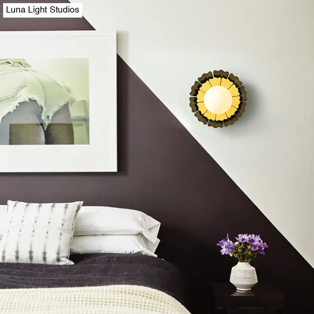 A modern sunflower yellow wood wall sconce with matte white glass ball and dark brown petal-like outer rings for bedroom