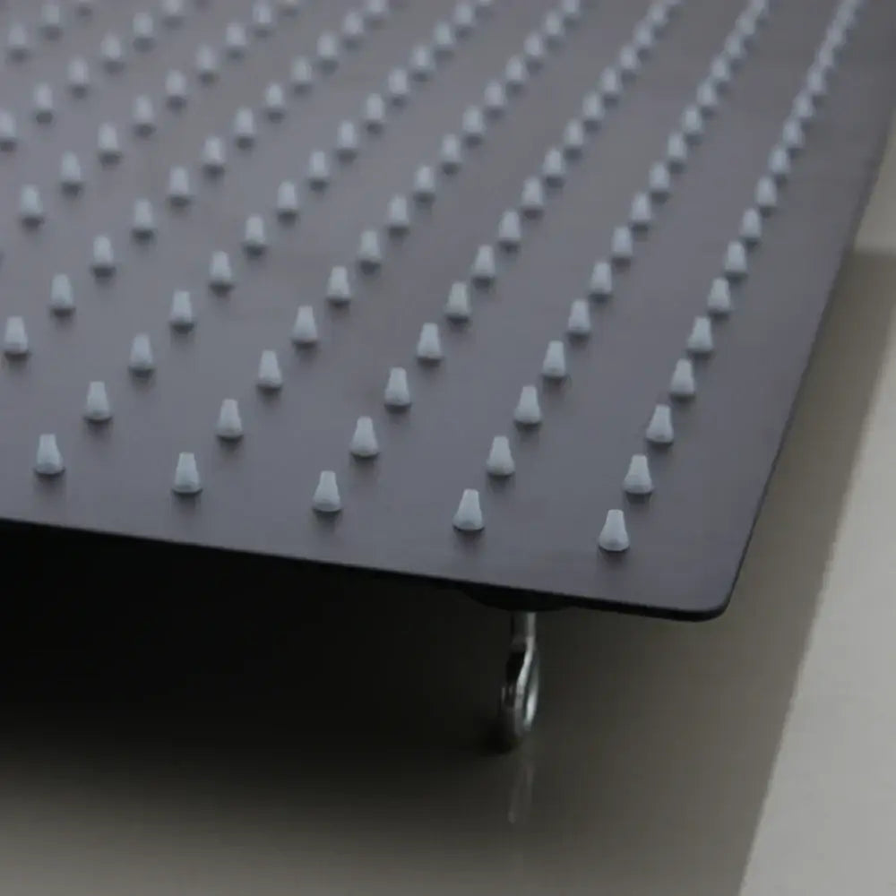 Black rectangular board with white plastic pegs and caster wheel showing the back side of a super slim matte black shower head