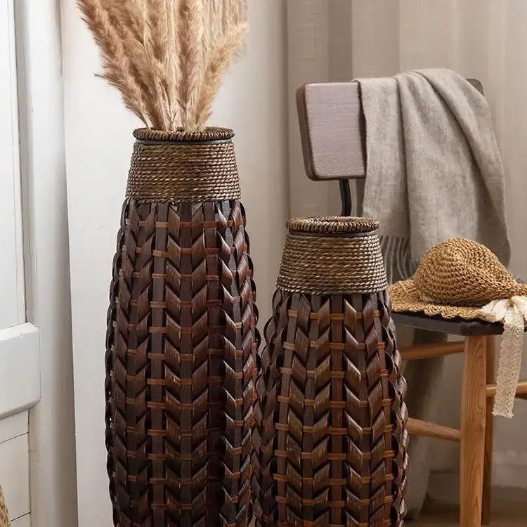 Two tall dark brown bamboo woven vases with herringbone pattern and rope rims holding dried pampas grass for living room decor