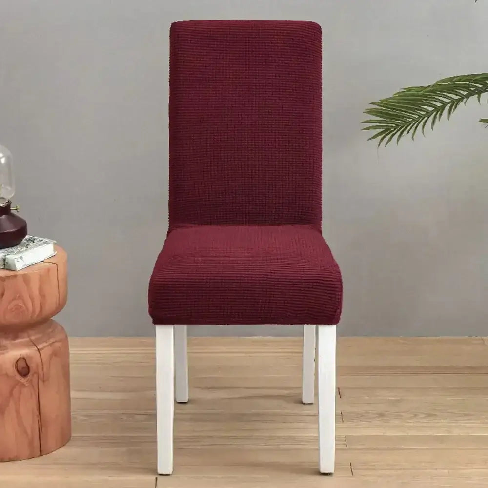 A burgundy corduroy chair cover snugly fits a white-legged dining chair, contrasting decorbites blue quilted chair covers