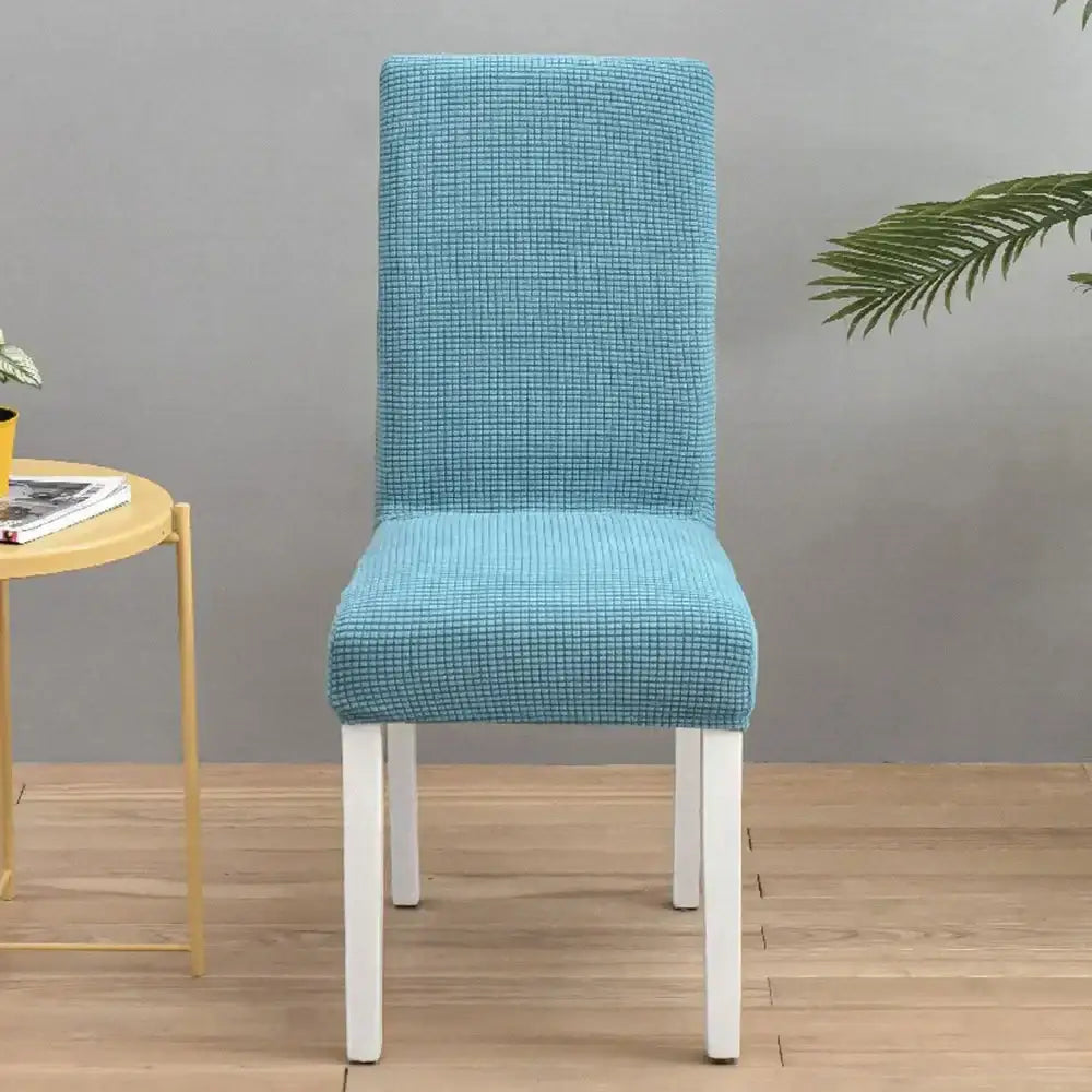 A teal blue quilted chair cover with stretch elastic material snugly fits a white dining chair for decorbites decor