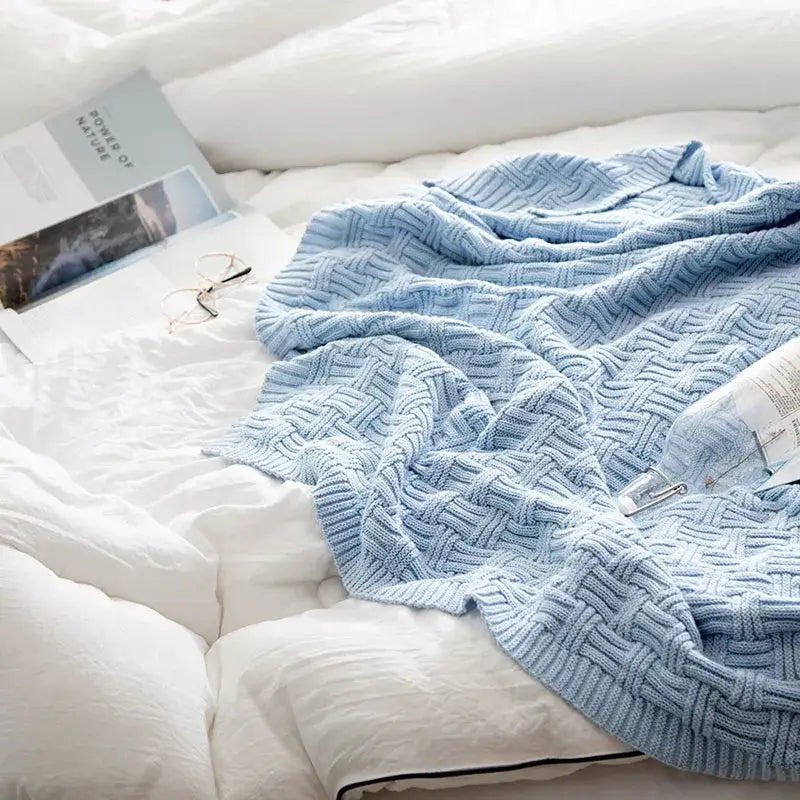 A light blue decorbites cozy jacquard blanket with textured knit pattern draped on white bedding for living room decor