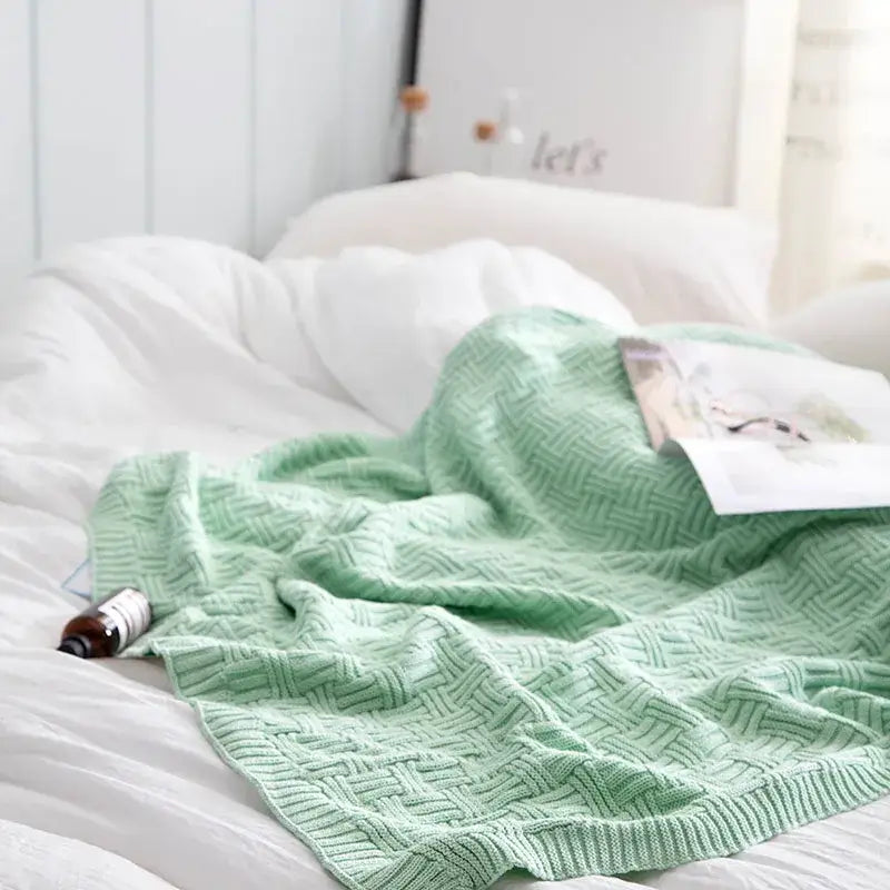 A soft mint green cozy jacquard blanket with textured herringbone pattern draped over white bedding by decorbites