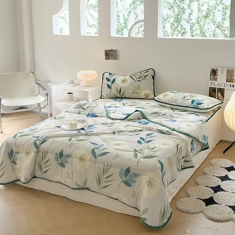 A cream-colored quilt with green and blue botanical print and subtle stitching in decorbites cool summer blanket set