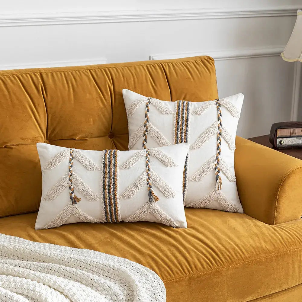 Cream-colored embroidered pillow covers with braided tassels on mustard sofa for decorbites boho tufted decor