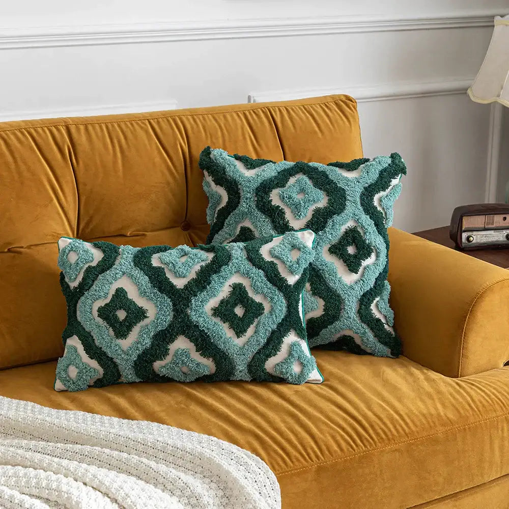 Two plush teal and dark green decorbites boho tufted pillow covers with geometric pattern on mustard velvet sofa