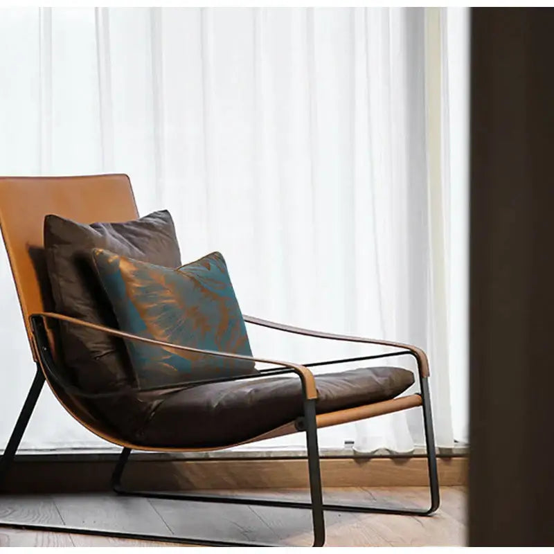 A sleek lounge chair with tan leather frame and teal and gold banana tree leaves jacquard cushion cover