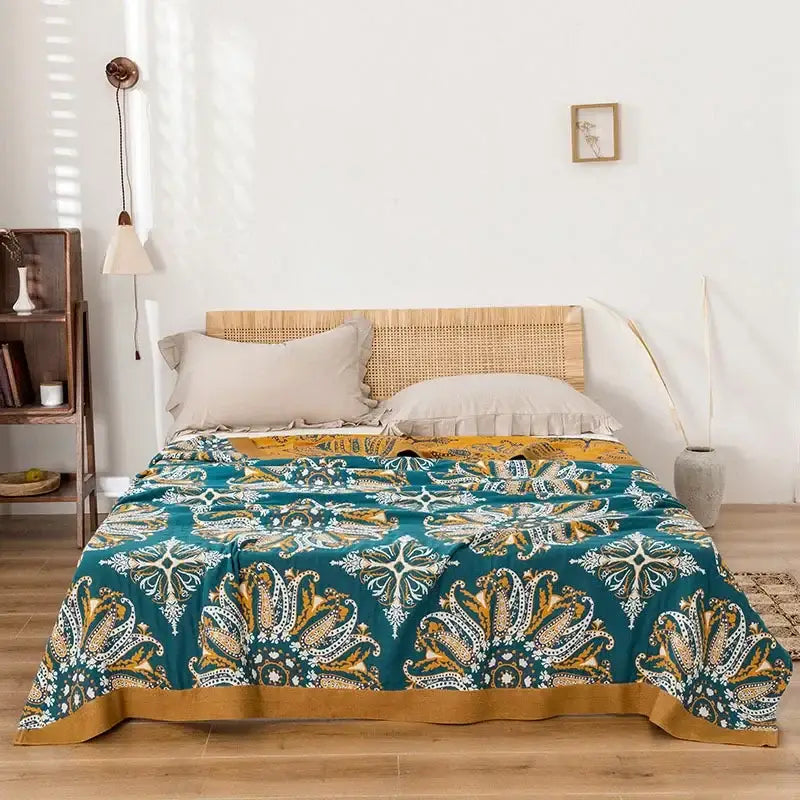 Teal and gold paisley decorbites bohemia cotton blanket displayed with a woven rattan headboard in the background