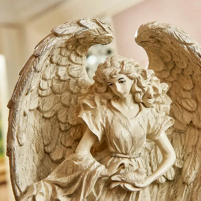 Beige prayer angel goddess statue with detailed feathered wings holding a small bird in teal and gold greek mythology style