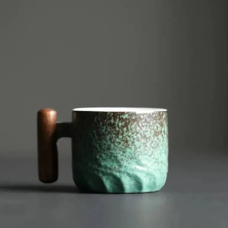 A ceramic coffee cup with teal gradient glaze, brown speckles, and a smooth wooden handle for kitchen use