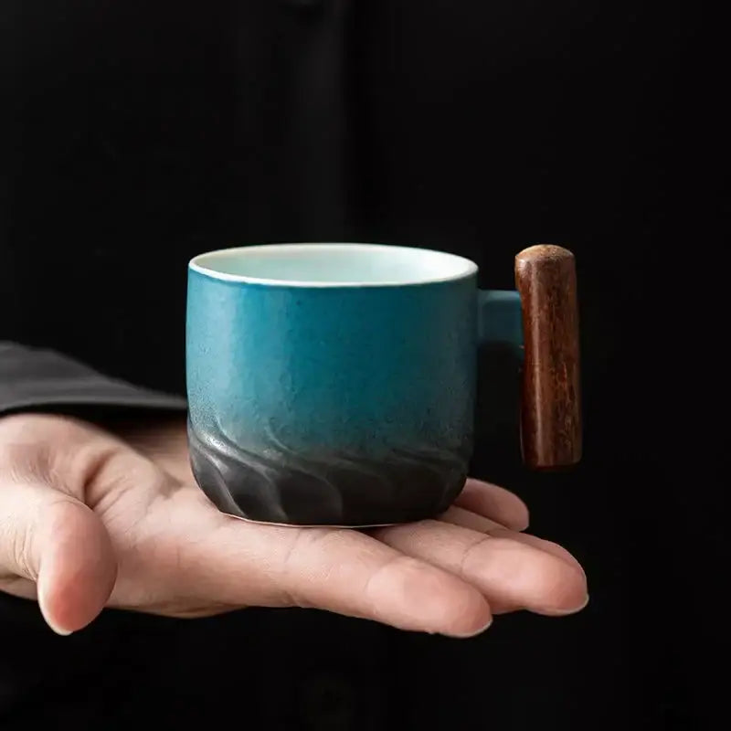 A ceramic coffee cup with teal gradient glaze and wooden handle held in hand for kitchen use