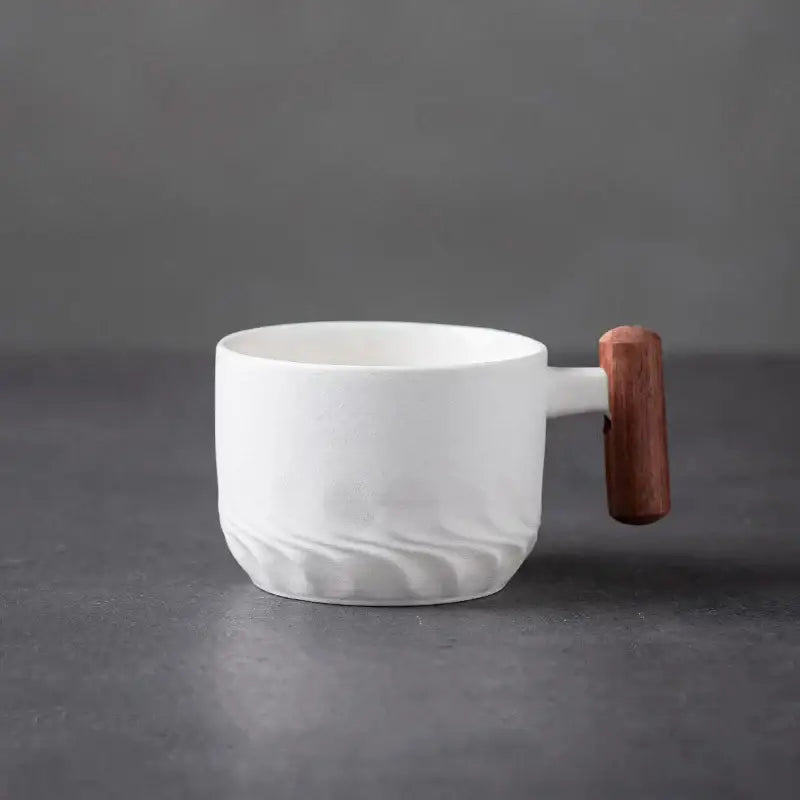 White ceramic coffee cup with textured wavy pattern and smooth wooden handle for kitchen use