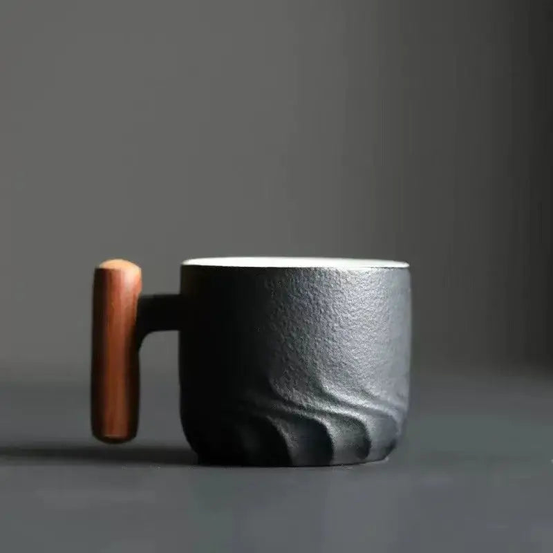 Black ceramic coffee cup with textured wavy surface, smooth white interior, gradient glaze, and warm wood handle