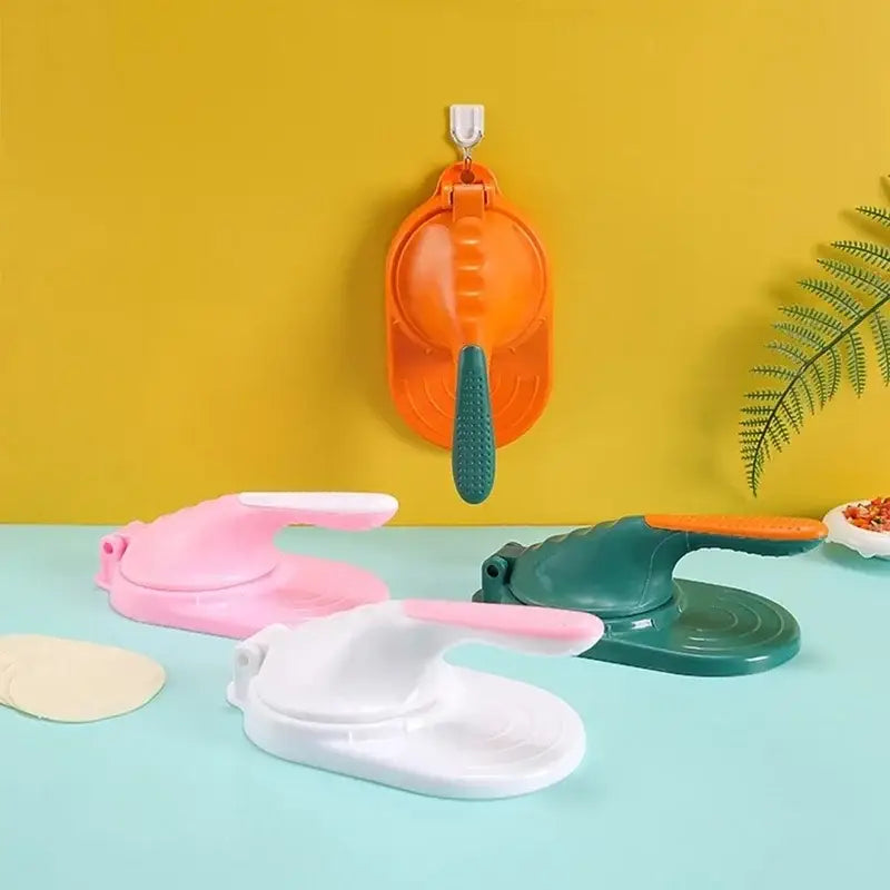 Orange plastic dough press tool with green textured handle hanging on wall for dumpling skin maker use