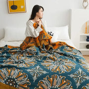 A cozy teal and orange paisley decorbites geometric cotton gauze summer blanket draped over a woman in bed