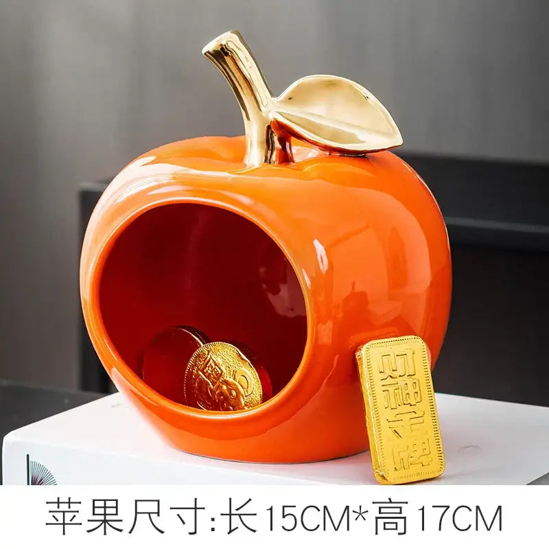 Vibrant orange ceramic apple storage box with gold stem and open interior holding coins for living room storage
