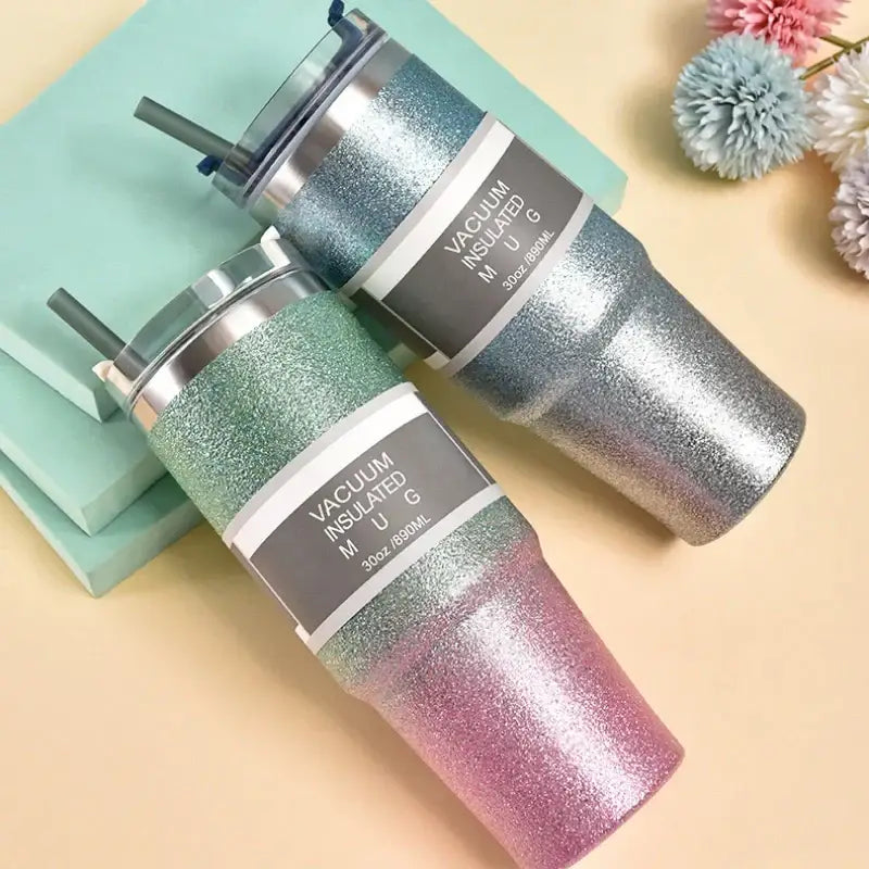 Two glittery decorbites coffee cup thermos mugs in teal to pink gradient and silver with stainless steel lids and straws