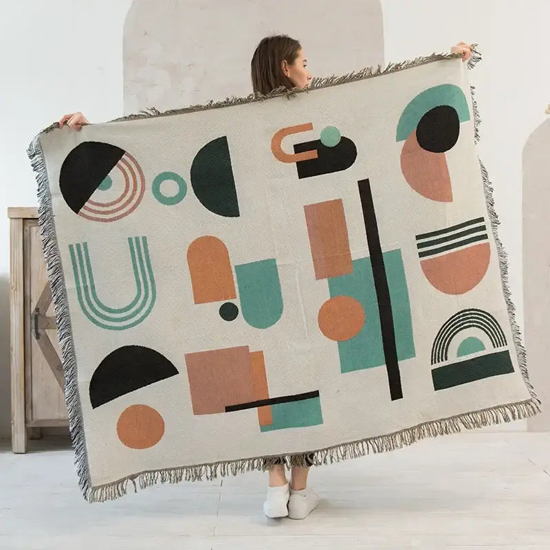 A cream-colored decorbites knitted nordic outdoor sofa throw with teal geometric pattern and fringed edges
