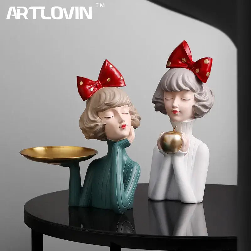 Two stylized bowknot girl resin figurines in teal and white with red bows holding a gold tray and golden apple decorbites bowknot girl