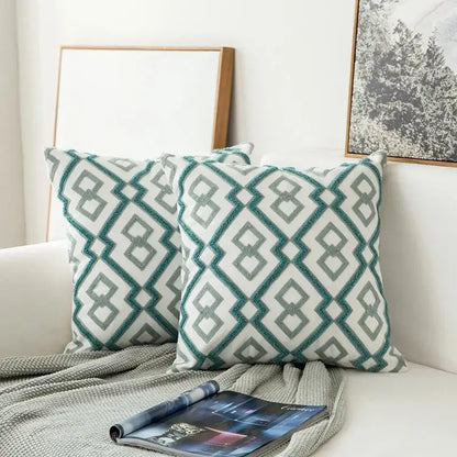 Two square teal and white cushion covers with embroidered geometric floral pattern and textured borders for living room
