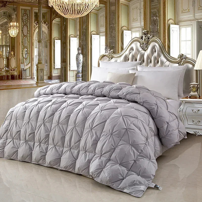 A plush light gray quilted comforter with diamond stitching made of white goose down for warmth and comfort on an ornate bed
